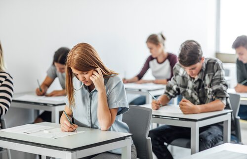 Weiterbildung im Projektmanagement: Absolvent/-innen sitzen an Schreibtischen und legen eine schriftliche Prüfung ab.