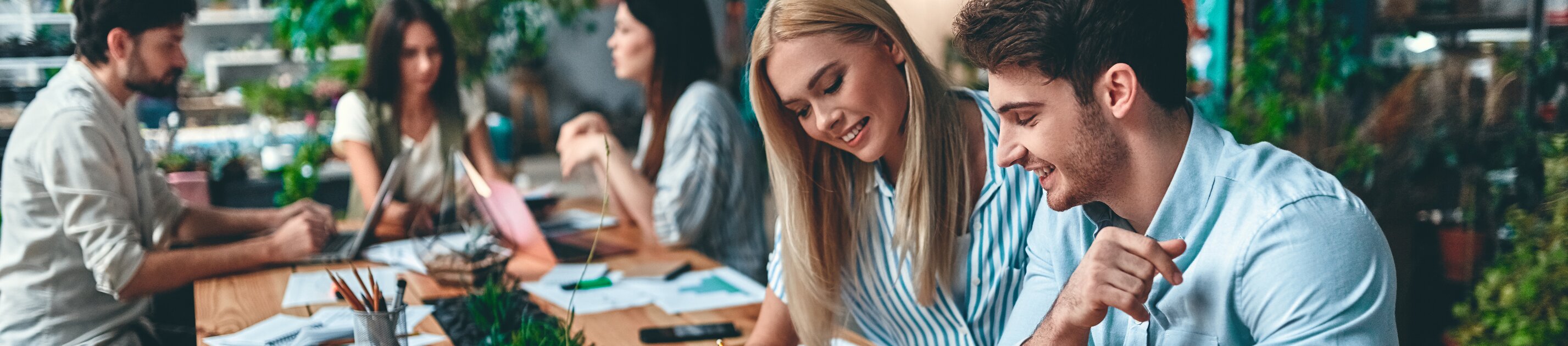 Team arbeitet gemeinsam an Projekten am großen Holztisch im modernen Büro