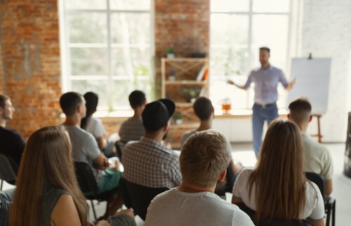 Teilnehmende sitzen im Seminarraum und hören Präsentation eines Trainers