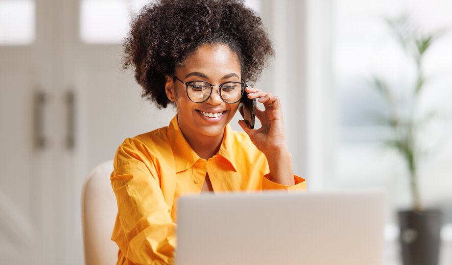 Frau arbeitet lächelnd am Laptop und telefoniert im modernen Homeoffice