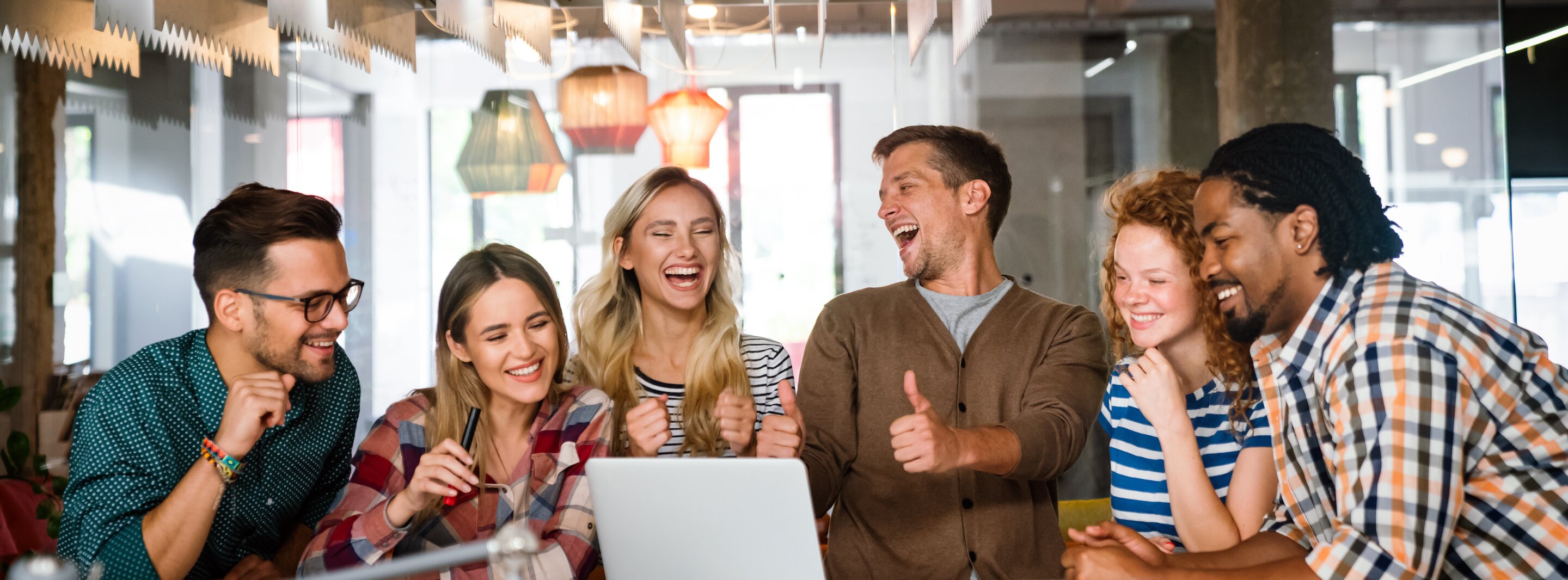 Team lacht und feiert erfolgreichen Meilenstein bei kreativem Meeting im modernen Büro