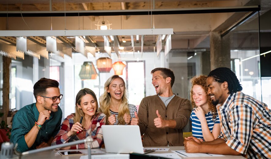 Team lacht und feiert erfolgreichen Meilenstein bei kreativem Meeting im modernen Büro