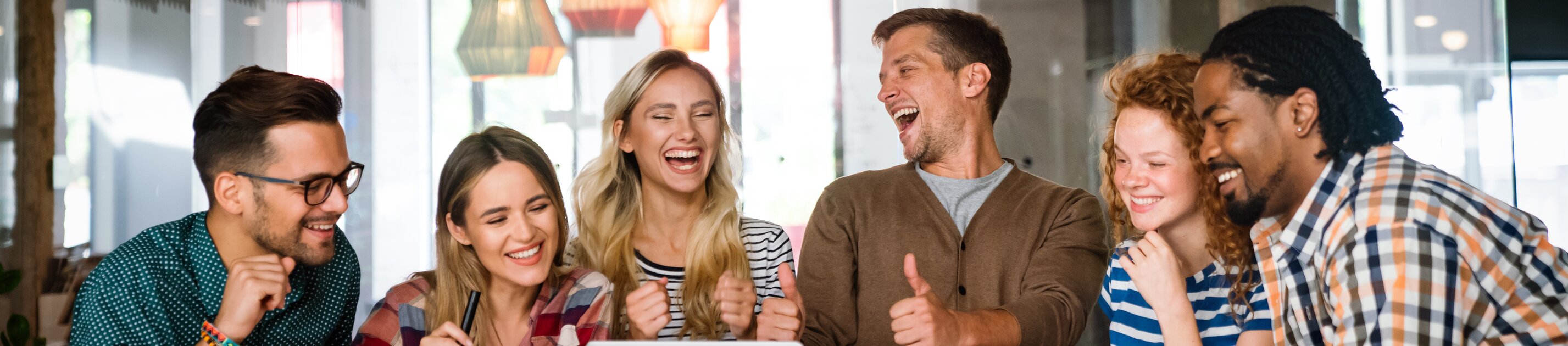 Team lacht und feiert erfolgreichen Meilenstein bei kreativem Meeting im modernen Büro