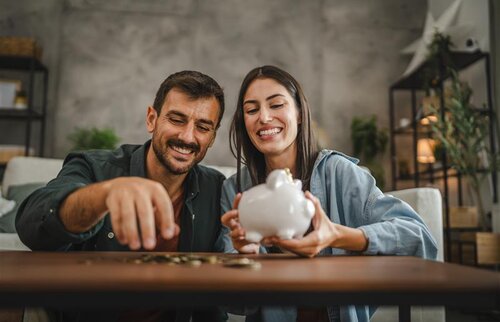 Paar legt gemeinsam Geld in ein Sparschwein als Symbol für finanzielle Förderung durch die Agentur für Arbeit.