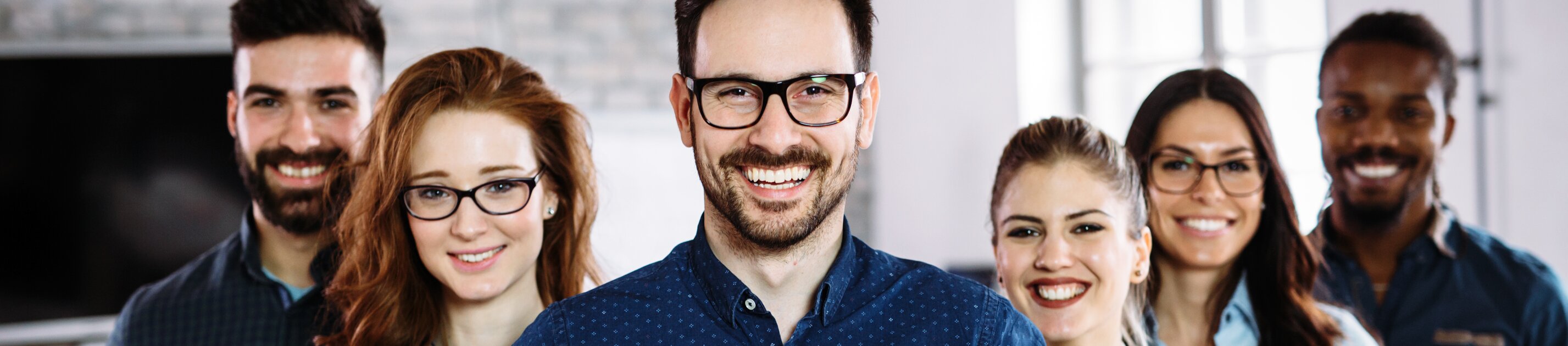 Gruppe junger Berufstätiger lächelt motiviert in modernem Büro und hält Unterlagen in der Hand