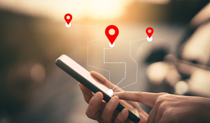 Das Bild zeigt eine Person, die ein Smartphone bedient, während darüber grafisch Navigations-Pins und eine gestrichelte Route eingeblendet sind: eine Darstellung für GPS-Navigation oder Standortverfolgung.
