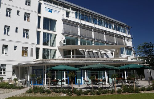 IHK Akademie München mit moderner weißer fassade und sonniger terrasse mit sonnenschirmen