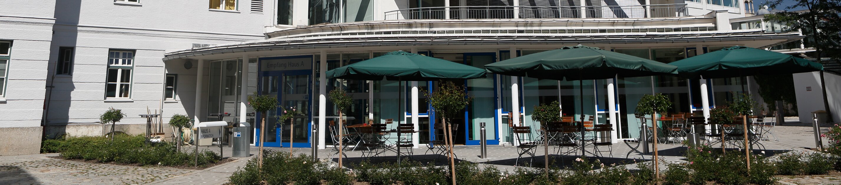 IHK Akademie München mit moderner weißer fassade und sonniger terrasse mit sonnenschirmen