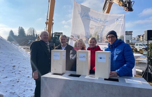 Personengruppe bei der Grundsteinlegung des Campus Chiemgau in Traunstein mit Zeitkapseln auf winterlicher Baustelle