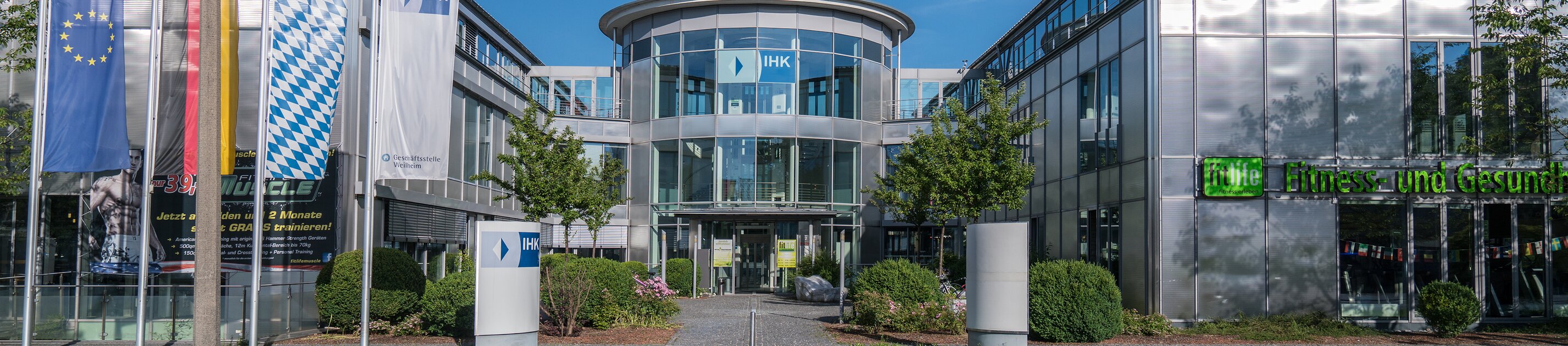 ihk akademie hauptgebäude mit glasfassade und fahnen bei blauem himmel
