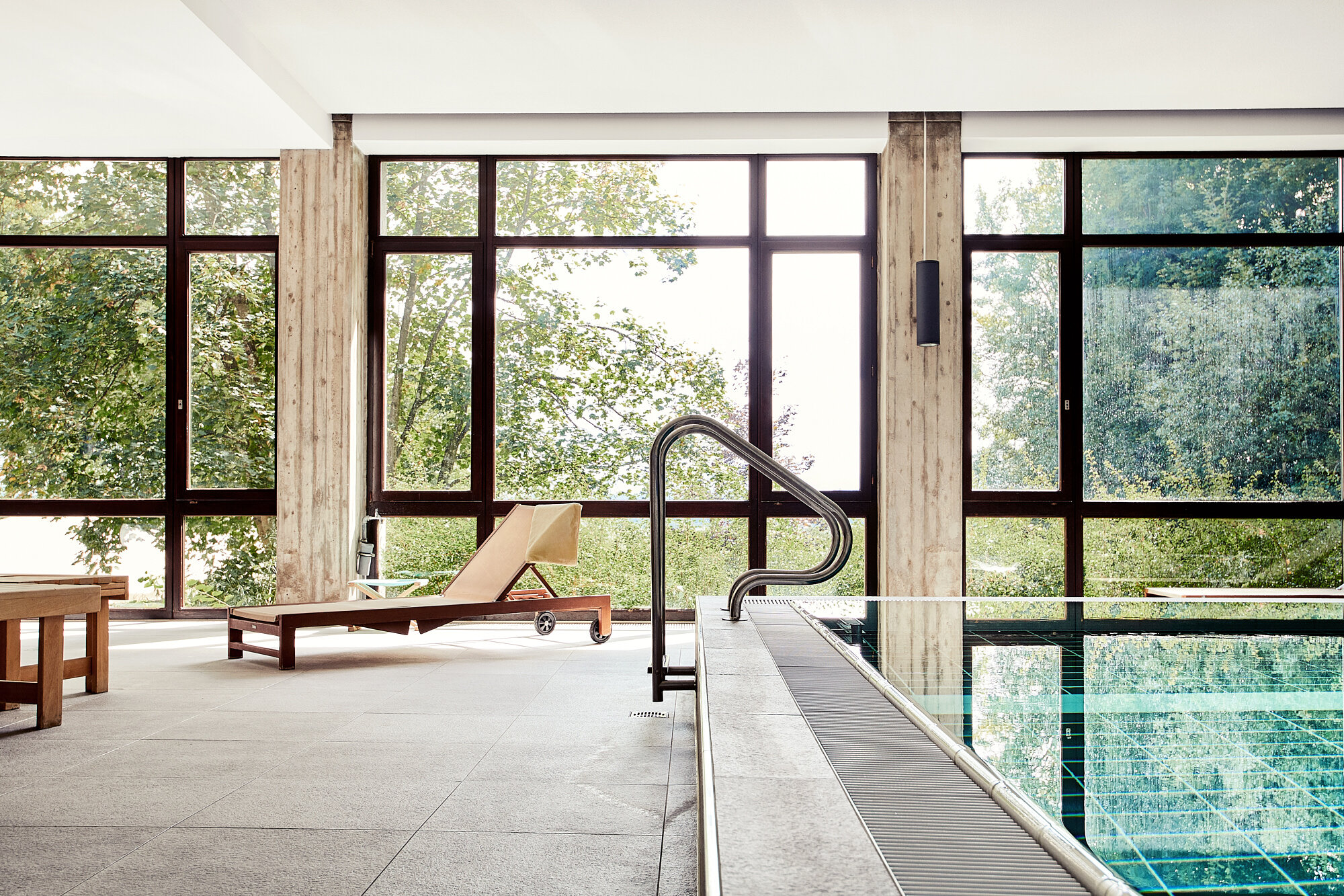 Helles Hallenbad der Akademie Westerham mit Liegestuhl und großen Panoramafenstern mit Blick ins Grüne – ein Ort zum Entspannen und Auftanken