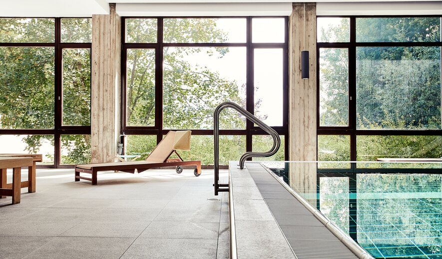 Ruhebereich am Indoor-Pool der IHK Akademie Westerham mit Liegestuhl und großen Panorama-Fenstern ins Grüne