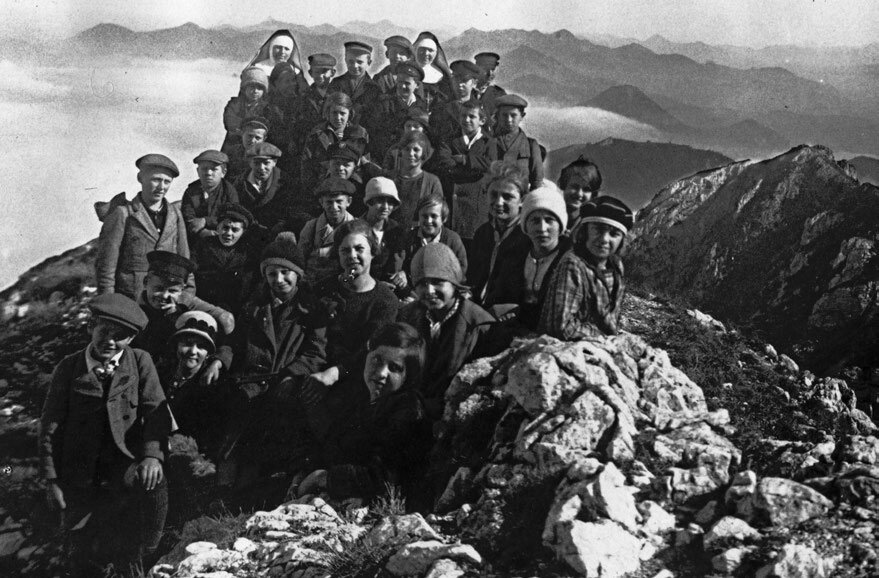 Schwarz-Weiß-Aufnahme einer Kindergruppe mit Betreuern bei einer Bergwanderung in den Alpen