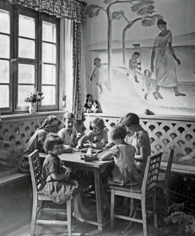 Schwarz-Weiß-Fotografie von Kindern beim Essen im Speisesaal des Kinderkurheims Westerham, mit Wandmalerei und Tageslicht durch große Fenster