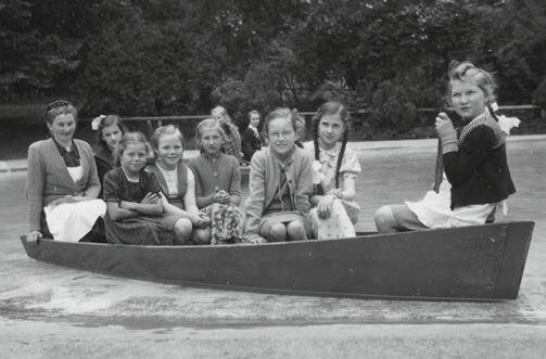 Schwarz-Weiß-Aufnahme von Kindern und einer Betreuerin in einem Ruderboot im Kinderkurheim Westerham, umgeben von Bäumen