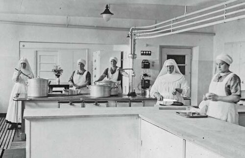 Schwarz-Weiß-Fotografie der Klosterküche im Kinderkurheim Westerham: Nonnen und Küchenpersonal bereiten an großen Töpfen eine Mahlzeit zu