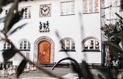 Fassade der IHK Akademie Westerham mit markanter Sonnenuhr über dem Eingangsportal und kunstvoll gestalteter Holztür, Symbol für die neue Nutzung des ehemaligen Kinderkurheims als Bildungsstätte.