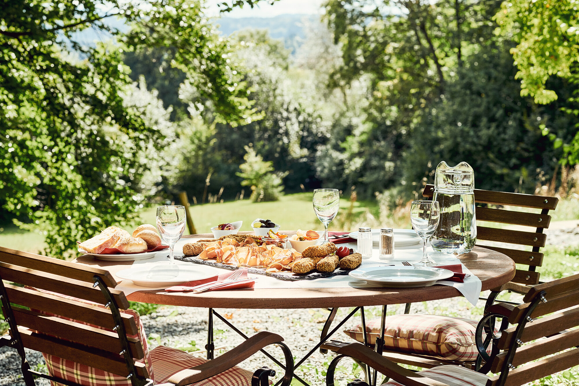 Frühstückstisch im Garten der Akademie Westerham mit frischen Brötchen, Croissants und Obst in der Morgensonne