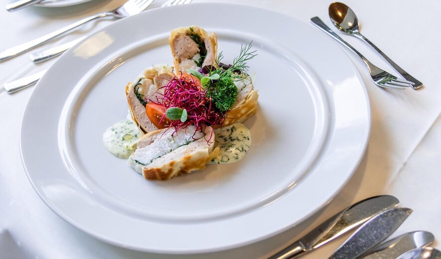 Fein angerichtetes Gourmetgericht auf weißem Teller mit Kräutern und Sauce in elegant gedecktem Restaurant setting