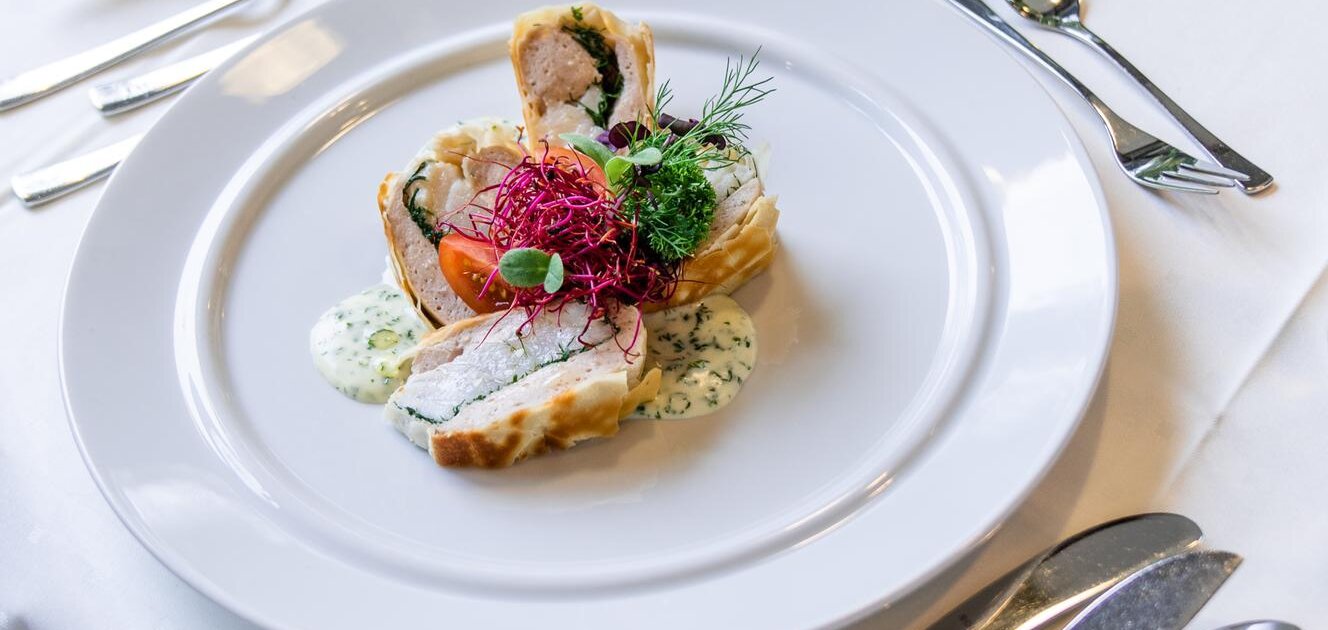 Fein angerichtetes Gourmetgericht auf weißem Teller mit Kräutern und Sauce in elegant gedecktem Restaurant setting