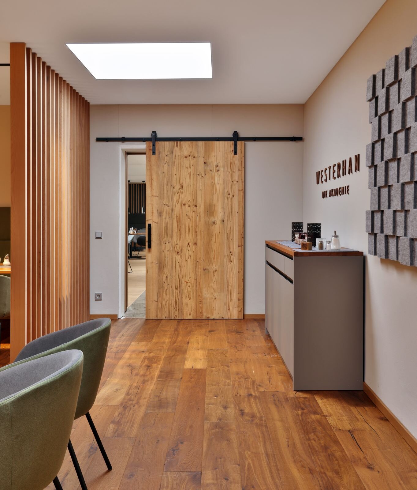 Moderner, warm gestalteter Innenraum mit Holzboden, einer großen Holz-Schiebetür, Akustikwand, seitlichem Sideboard und gemütlichen Sitzmöbeln im Kaminstüberl Westerham.