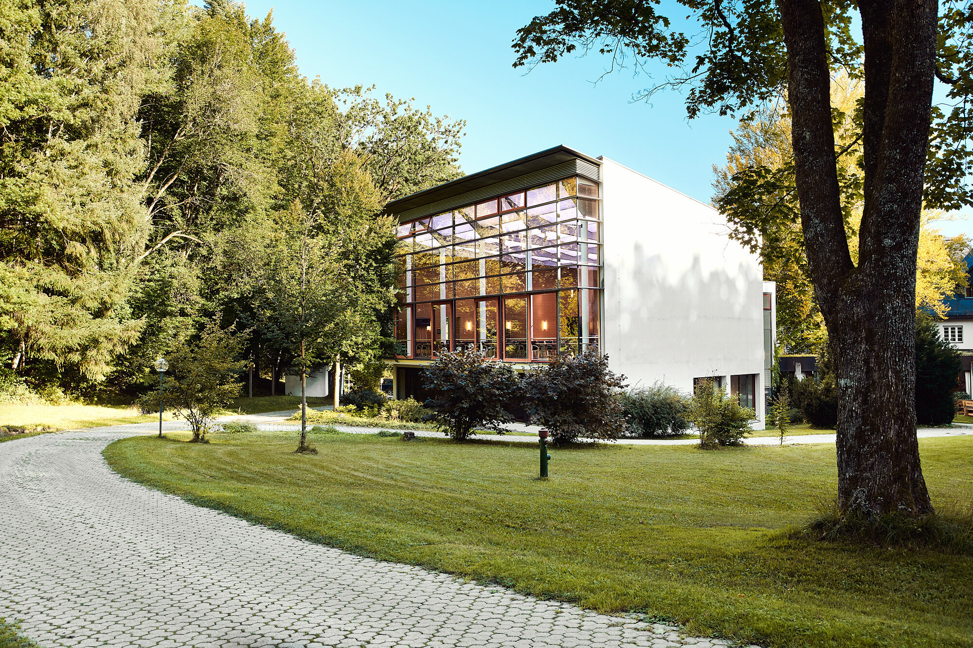 Tagungsgebäude der Akademie Westerham mit großer Glasfront im Grünen umgeben von Bäumen und Gartenweg