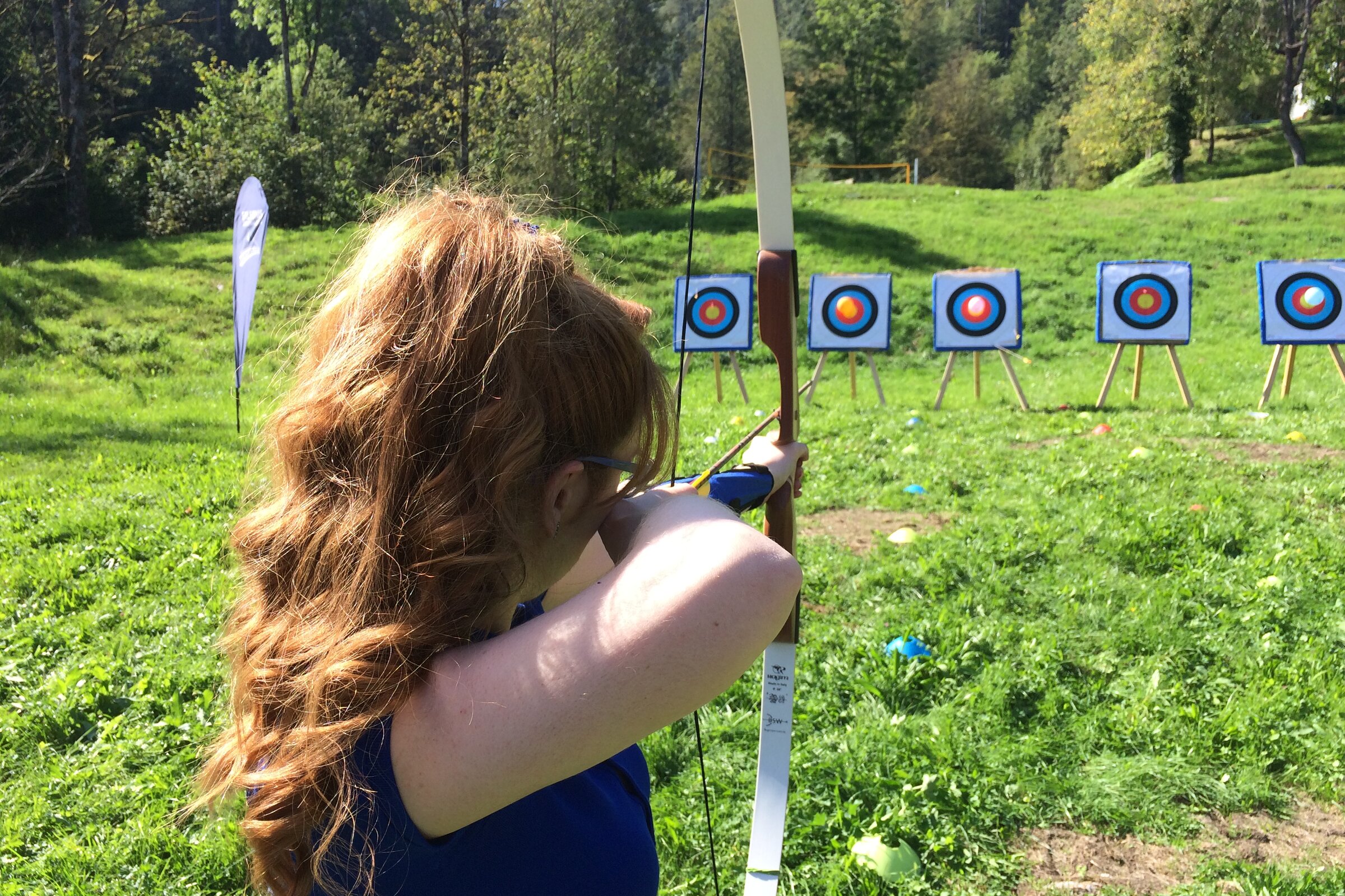 Teilnehmerin zielt mit Pfeil und Bogen auf Zielscheiben auf einer Wiese bei der Akademie Westerham