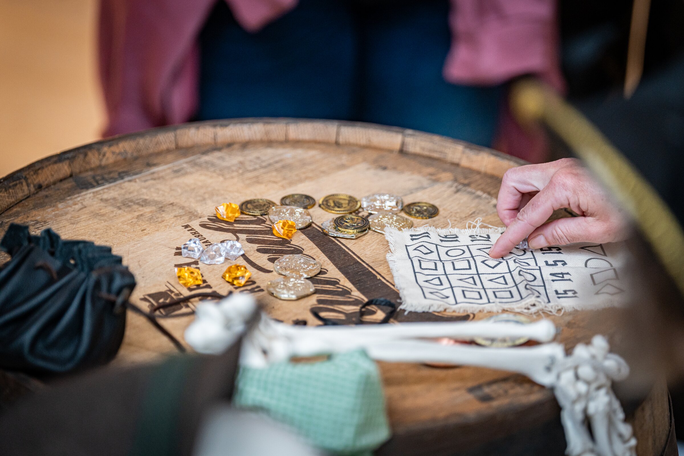 Nahaufnahme eines hölzernen Fasses mit Goldmünzen, Würfeln und einem Rätselzettel
