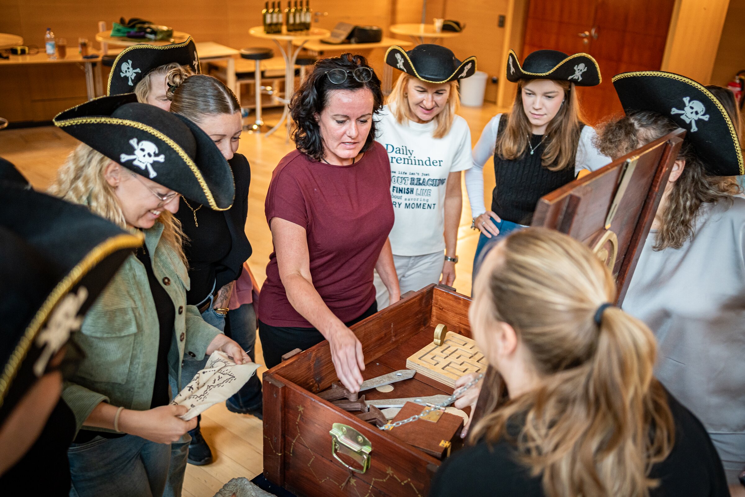 Eine Gruppe von Teilnehmenden mit Piratenhüten steht um eine geöffnete Schatztruhe und löst gemeinsam Rätsel
