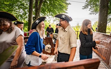 Gruppe von Menschen mit Piratenhüten lacht und spricht bei einem Outdoor-Teamevent in Westerham