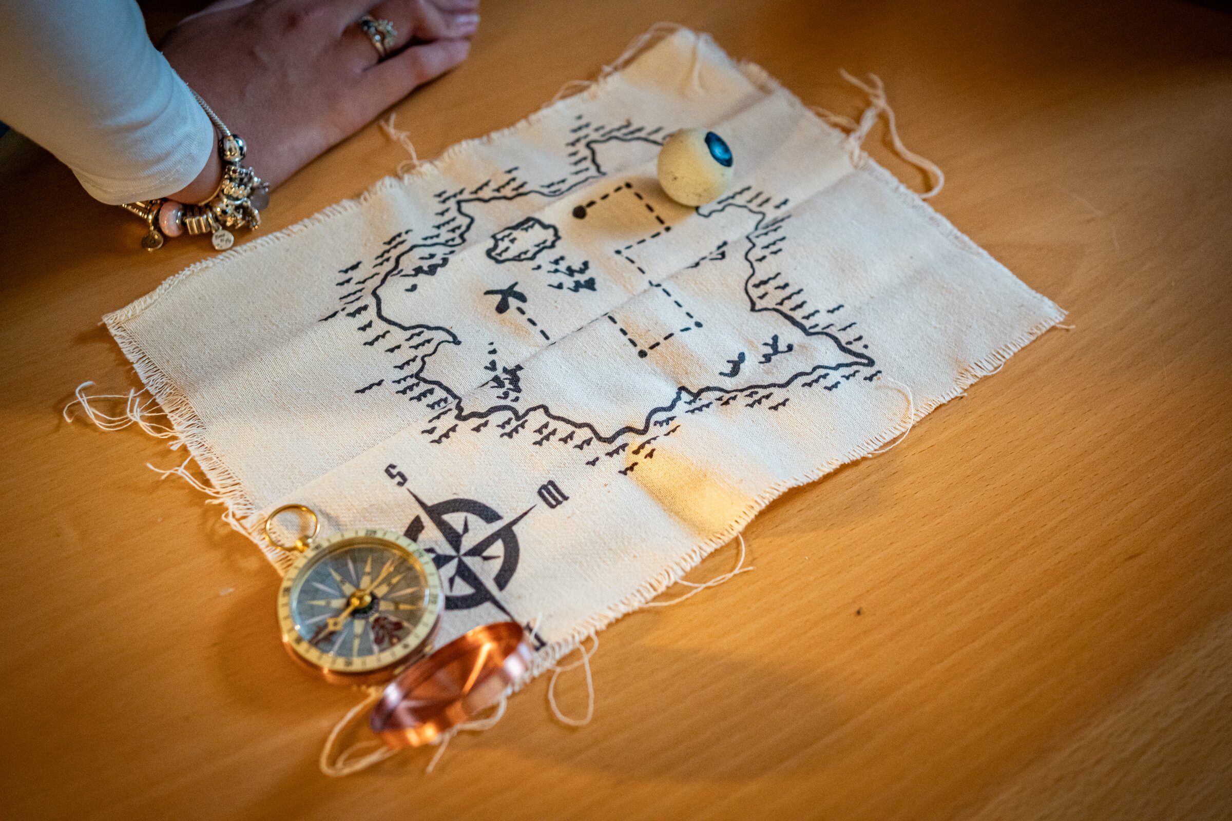 Nahaufnahme einer handgezeichneten Schatzkarte mit Kompass und Rätselutensilien auf einem Holztisch