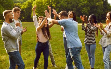 Gruppe von Kolleginnen und Kollegen lacht und klatscht sich beim Teamtraining draußen im Grünen ab – Teamtrainings in Westerham