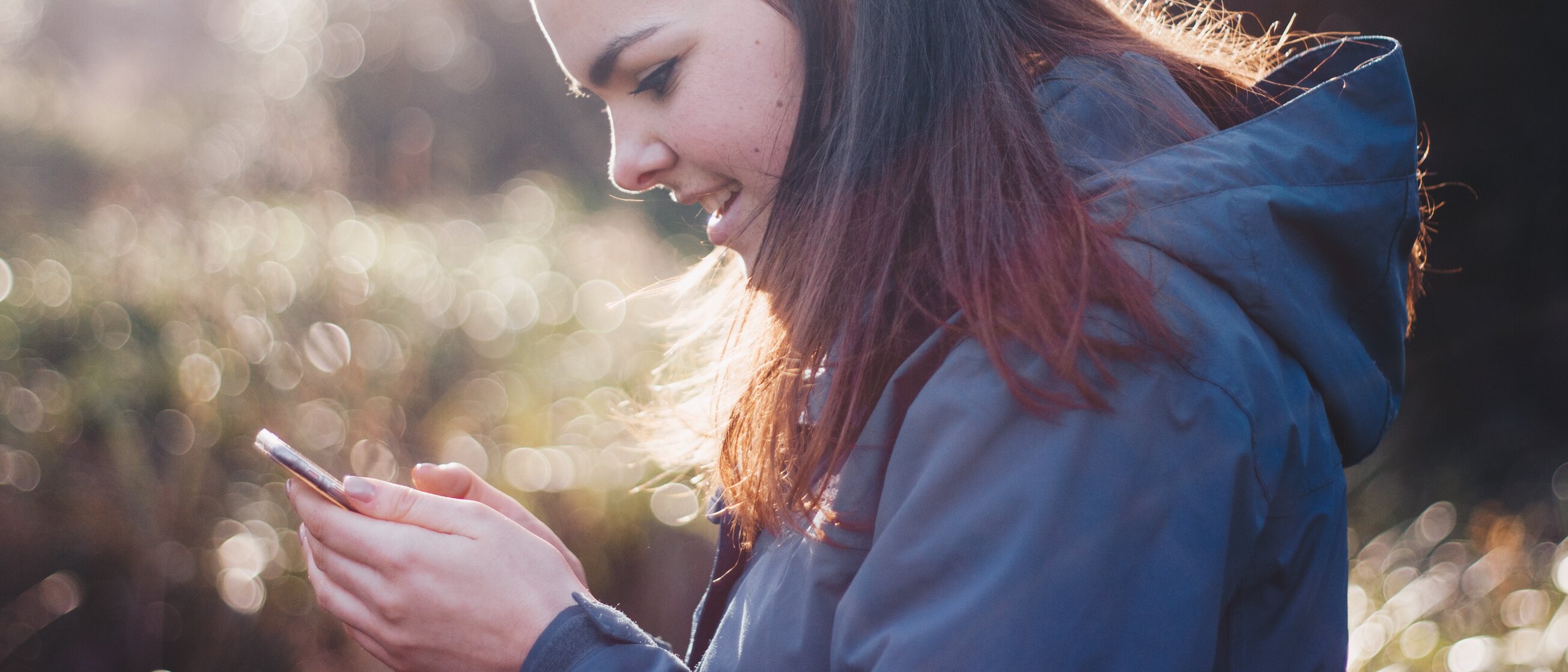 Frau steht im Freien und schaut konzentriert auf ihr Smartphone – GPS-Rallye-Teamevent in der Natur rund um die IHK Akademie Westerham