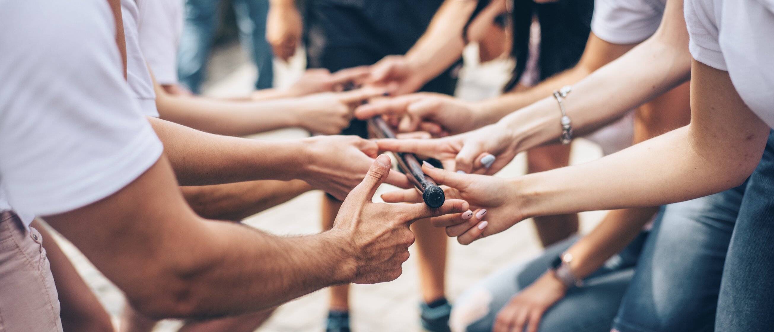 Team hält gemeinsam einen Stab und stärkt damit Zusammenarbeit und Teamgeist bei einer Outdoor-Übung.