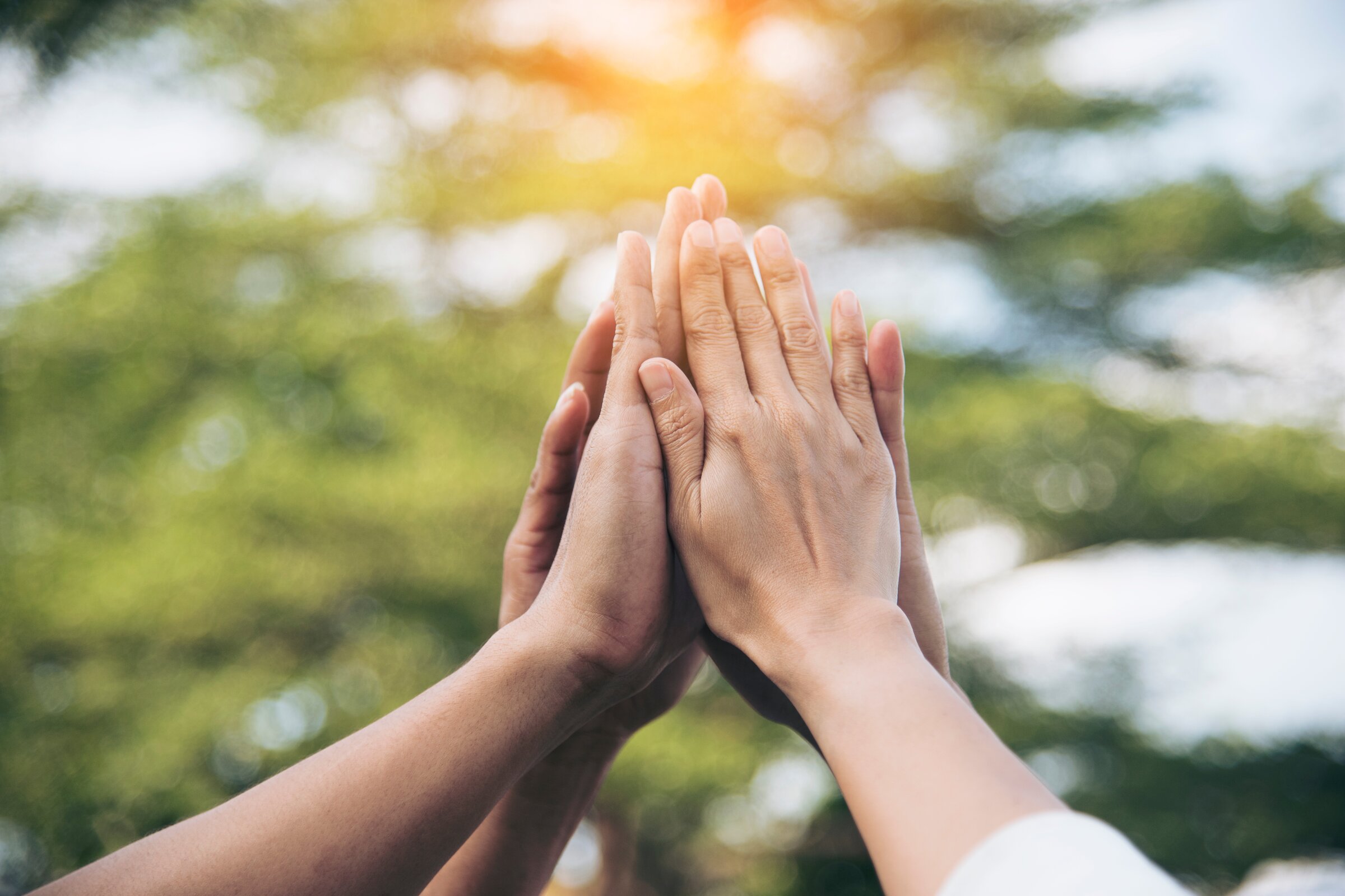 Team gibt sich draußen ein gemeinsames High-Five als Zeichen für Zusammenhalt und Motivation