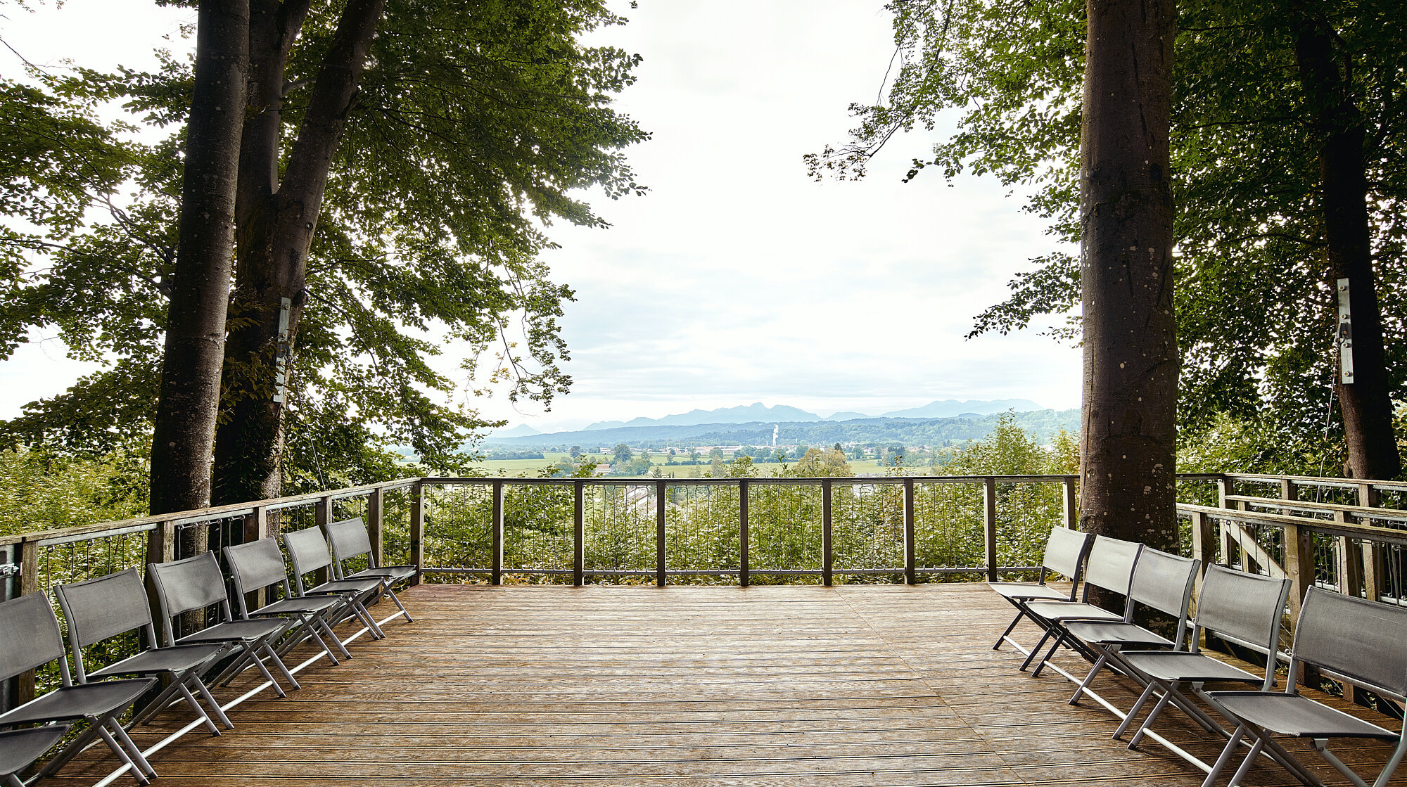 Holzplattform mit Sitzbänken zwischen Bäumen und Blick über die hügelige Landschaft – Ort für Seminare und Teamevents der IHK Akademie Westerham