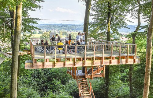 Seminargruppe auf einer erhöhten Holzplattform im Wald mit Panoramablick, ideal für außergewöhnliche Tagungen und inspirierende Team-Events.