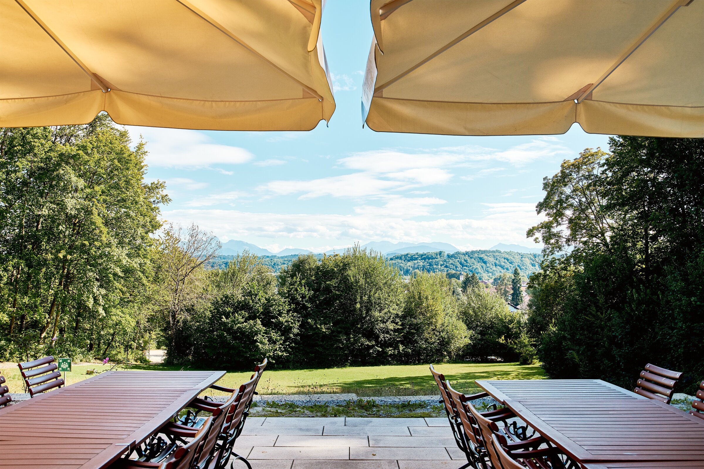Sonnenterrasse des Tagungshotels Westerham mit Panoramablick auf das Alpenvorland – gemütliche Sitzplätze unter Sonnenschirmen mit Blick auf grüne Wälder und Berge