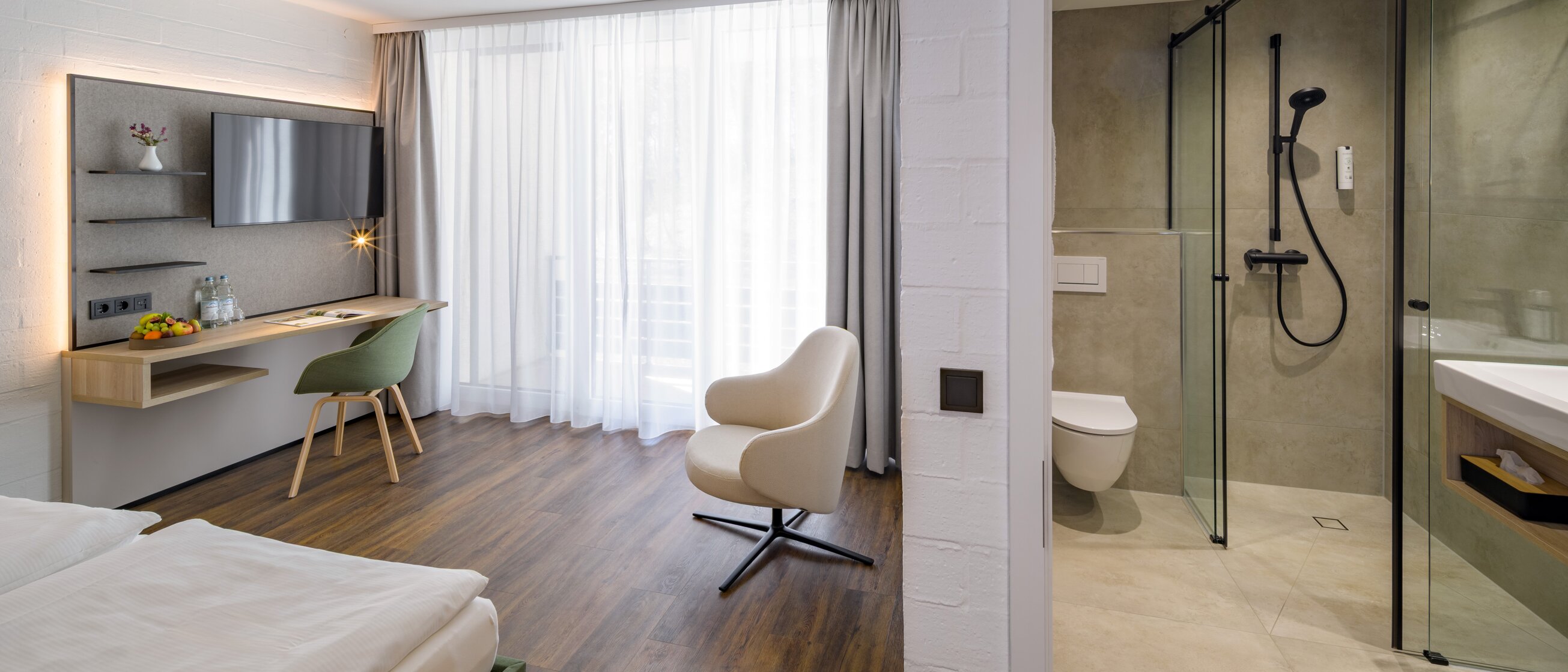 Ein stilvolles, lichtdurchflutetes Hotelzimmer mit modernem Bad, gemütlicher Sitzecke und elegantem Arbeitsbereich.