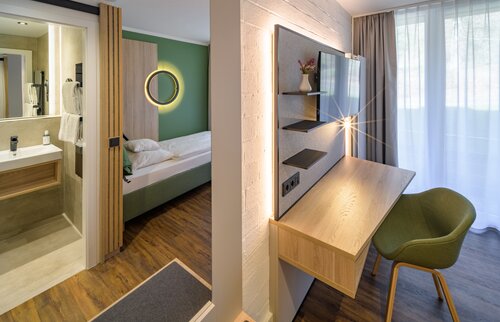 Modern eingerichtetes Einzelzimmer in der Akademie Westerham mit Schreibtisch, Einzelbett, Balkonzugang und stilvoller Beleuchtung