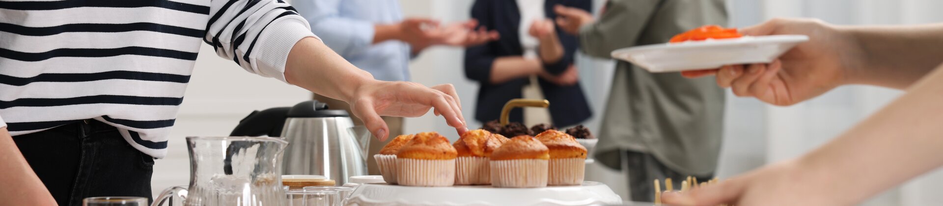 Ein reichhaltiges Buffet mit Gebäck, Aufschnitt und Säften, während sich im Hintergrund mehrere Personen ungezwungen unterhalten.