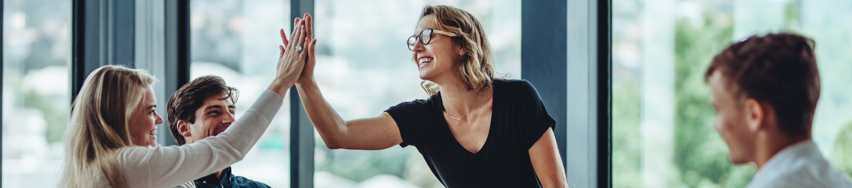 Zwei Personen geben sich lachend ein High-Five, während ihre Kolleginnen und Kollegen am Konferenztisch erfreut zusehen.