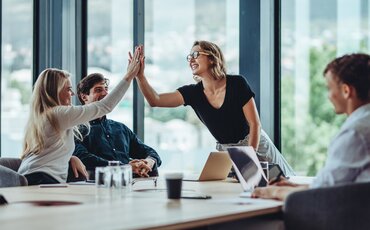 Team feiert Erfolg mit High-Five im Meetingraum – Symbol für erfolgreiche Projektkoordination und Zusammenarbeit.