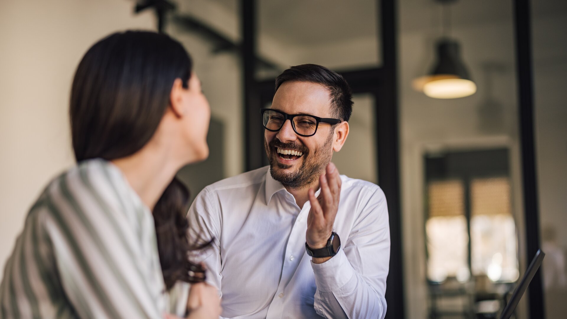 Ein Mann und eine Frau sitzen sich in einem Büro gegenüber, unterhalten sich angeregt und lachen gemeinsam.