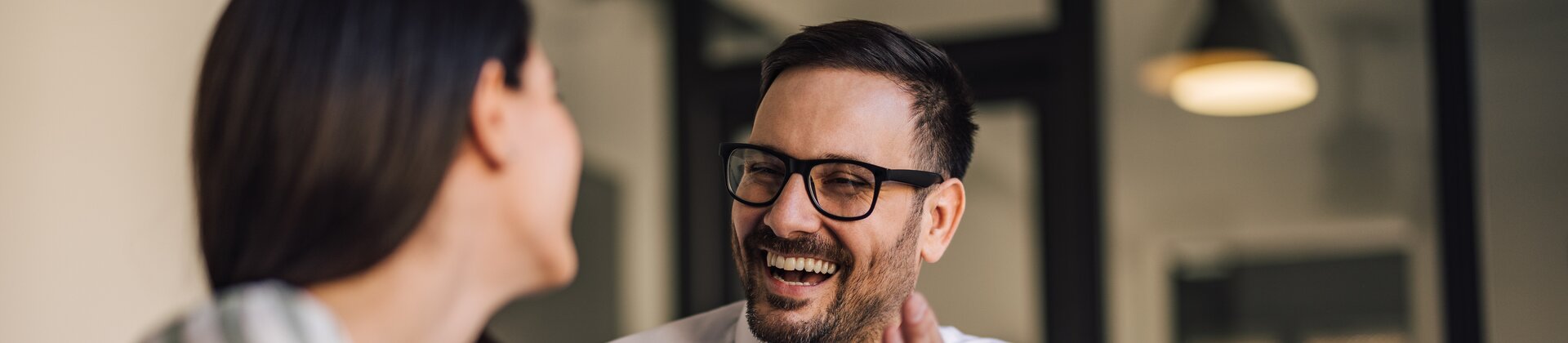 Ein Mann und eine Frau sitzen sich in einem Büro gegenüber, unterhalten sich angeregt und lachen gemeinsam.