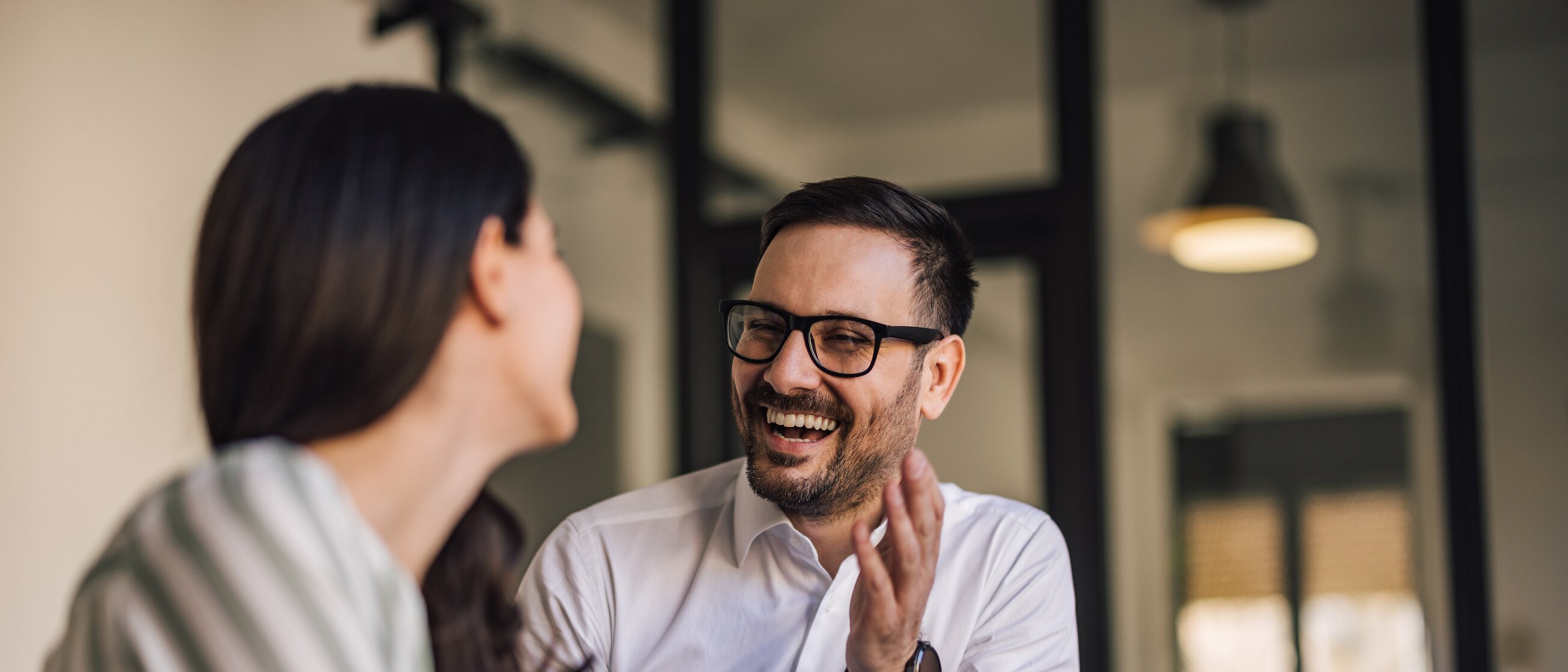 Zwei Personen unterhalten sich im Büro und lachen – steht für erfolgreiche Kommunikation und persönliche Weiterentwicklung.