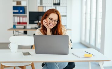 Frau arbeitet lächelnd am Laptop im modernen Büro – Symbol für effiziente Büroorganisation und Assistenz