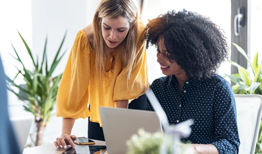 Zwei Personen arbeiten gemeinsam an Laptop und Tablet in einem hellen und modernen Büro.