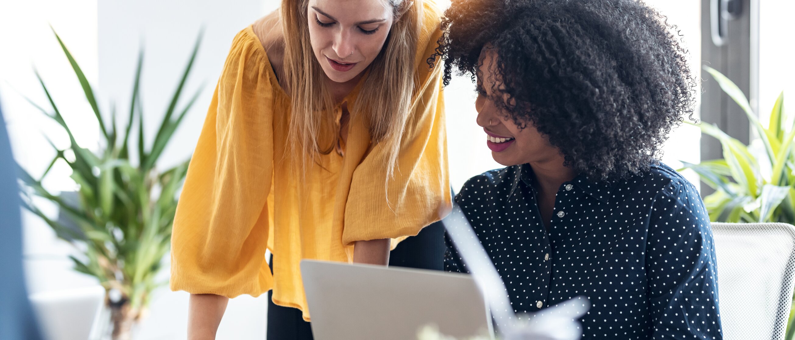 Zwei Frauen arbeiten gemeinsam am Laptop und lächeln – Symbol für erfolgreiche Kommunikation und Zusammenarbeit im Berufsalltag.