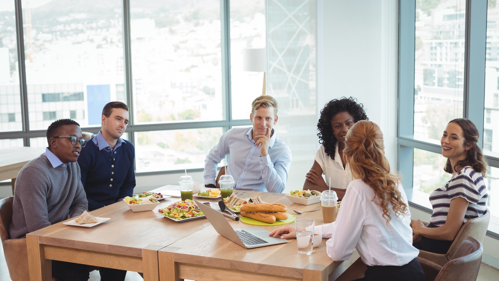 Eine Gruppe von Menschen sitzt gemeinsam an einem Tisch zu einem ungezwungenen Business-Lunch und bespricht etwas in entspannter Atmosphäre.